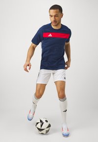 Navy blue athletic t-shirt with red horizontal stripe, paired with white shorts. Player is dribbling a black-and-white soccer ball.