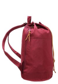 Punainen sylinterimäinen reppu, jossa on nyörisuljenta, sivutasku vetoketjulla ja säädettävät olkahihnat.