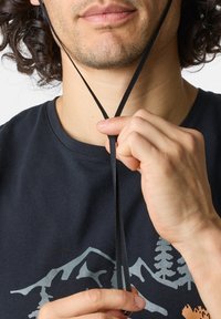 I lacci neri sono fissati al collo, in contrasto con una t-shirt blu-nera che presenta una grafica di montagne e alberi.