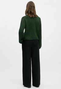 Mørkegrøn textured sweater med lange ærmer, parret med højtsiddende sorte stribede bukser. Sweateren har en afslappet pasform.