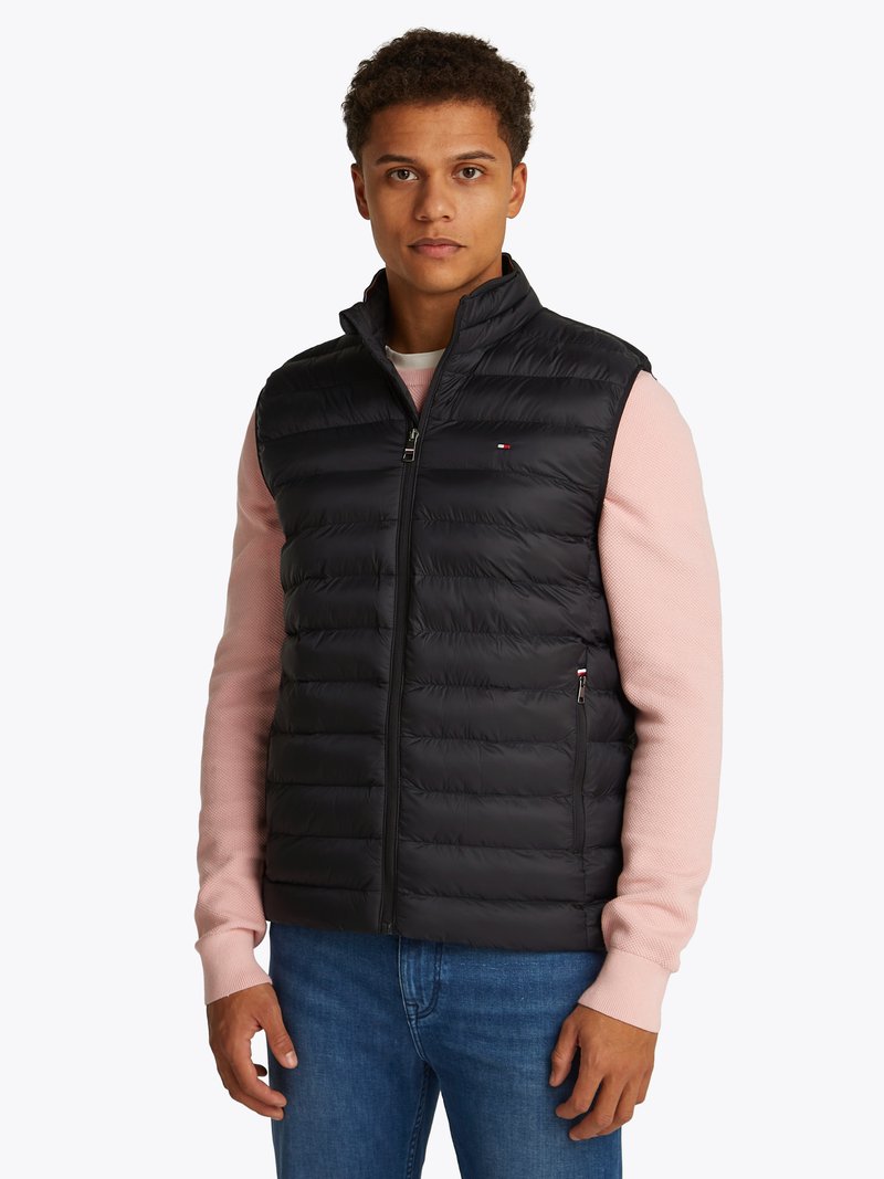 Colete puffer preto com gola alta, apresentando um fecho frontal completo e costuras horizontais. Usado sobre uma camisa de manga longa rosa claro.