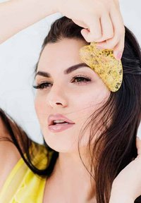 Żółte, przezroczyste narzędzie gua sha jest używane na twarzy, uwypuklając gładkie krawędzie i teksturowaną powierzchnię.