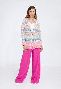 Blazer a fantasia multicolore con tonalità di rosa, blu e giallo, abbinato a pantaloni larghi in lino rosa e una maglietta bianca.