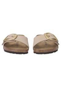 Infradito beige con una larga cinturino e una fibbia dorata. Soletta in sughero e suola in gomma texturizzata. Design aperto per respirabilità.