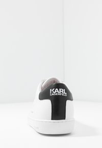 Bílé tenisky s černým koženým akcentem na patě. Mají strukturovaný povrch, gumovou podrážku a potisk "KARL LAGERFELD".