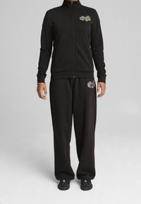 Chaqueta negro con cremallera y pantalones a juego, hechos de un tejido suave, con detalles bordados en ambas prendas y un corte relajado.