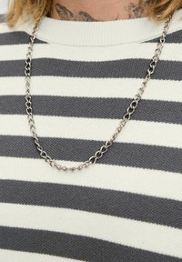 Silver chain necklace with alternating oval and twisted links, layered over a gray and white striped knit sweater.