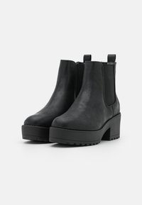Botas Chelsea negras hechas de cuero sintético texturizado, con un grueso tacón plataforma y paneles laterales elásticos para facilitar su uso.