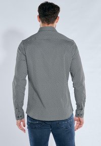 Schwarz-wei�ß gemustertes Langarmhemd mit Kragen, das ein geometrisches Design und geknöpfte Manschetten aufweist, getragen zu blauen Jeans.