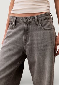 Harmaat farkut ovat rentoa mallia, hieman haalistuneet, perinteisellä viiden taskun mallilla ja napin suljennalla. Materiaali on sileä ja siinä on lievä kiilto.