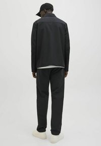 Schwarze Jacke mit glatter Textur, kombiniert mit passenden Hosen und weißen Sneakern. Mit Kragen und lockerer Passform. Rückansicht.