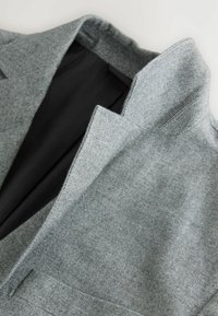 Siv herringbone blazer z notched ovratnikom. Notranjost z črno oblogo. Teksturen material s strukturirano zasnovo.
