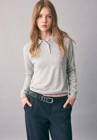 Polo grigio a maniche lunghe con colletto, caratterizzato da una texture a maglia. Abbinato a pantaloni blu scuro a righe sottili e una cintura nera con dettagli argentati.