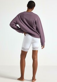 Lilla oversized sweatshirt med lange ærmer, kombineret med hvide shorts med blondetrim. Glat stof, afslappet pasform og blondeaccentdetalje.