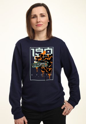 Sweat-shirt bleu marine avec un design graphique d'une voiture vintage agrémenté de coulures de peinture orange et noire ; coupe décontractée et manches longues.