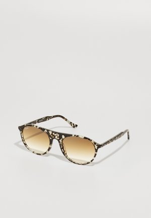 Γυαλιά ηλίου με πλαίσιο από ακρυλικό σε μαύρο και κρεμ σχέδιο, στρογγυλούς φακούς που μεταβαίνουν από σκούρο σε ανοιχτό καφέ, και λεπτούς βραχίονες.