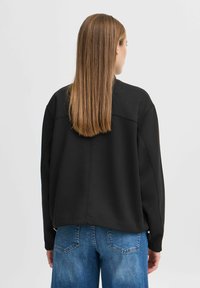 Svart sweatshirt med avslappnad passform, rund halsringning och texturerad yta, kombinerad med ljusblå denimjeans med klassisk skärning.