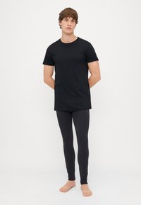 T-shirt noir à manches courtes associé à des leggings noirs ajustés ; tous deux en tissu lisse. Pas de motifs ni d'accents visibles. Modèle pieds nus.