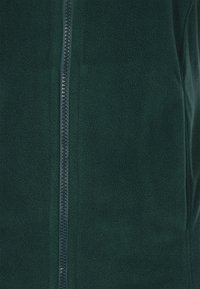 Fleecejacke in Dunkelgrün mit einem Frontreißverschluss und strukturiertem Stoff. Verfügt über einen glatten Reißverschlusslauf in der Mitte.