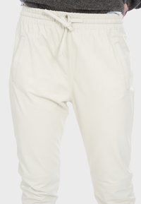 Białe dresy wykonane z miękkiego materiału, z elastycznym pasem i regulowanym sznurkiem. Posiadają dwie boczne kieszenie i opływowy kształt.