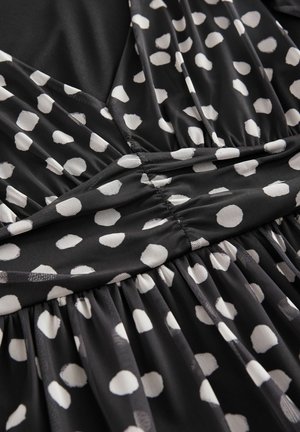 Rochie din țesătură neagră cu buline albe, având un corp strâns și detalii pliate ale fustei pentru un plus de textură.