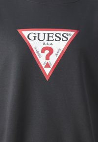 T-shirt noir avec un grand logo triangulaire rouge et blanc portant les inscriptions "GUESS" et "?". Le tissu semble lisse avec un col rond classique.