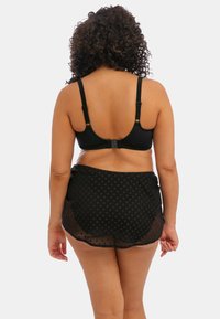 Soutien-gorge noir avec bretelles réglables et fermeture à crochet, associé à une jupe noire transparente avec un motif texturé, vue de dos.