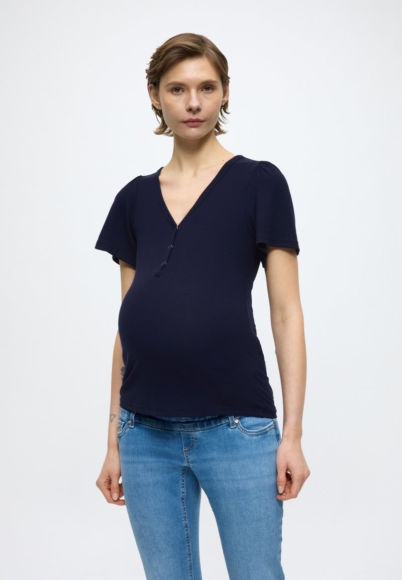 Camiseta premamá azul marino con mangas cortas, escote en V y detalles de botones. Confeccionada con tejido acanalado elástico, diseñada para ofrecer comodidad y un ajuste perfecto.