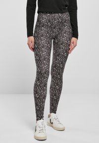 Leggings neri con un motivo astratto bianco, realizzati in tessuto elasticizzato; abbinati a sneakers bianche con dettagli verde.