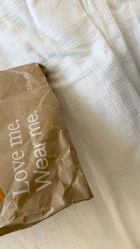 Smeđa papirnata vrećica s naboranom teksturom, s natpisom "Volite me. Nosite me." i Zalando logotipom, odložena na bijeloj teksturiranoj površini.