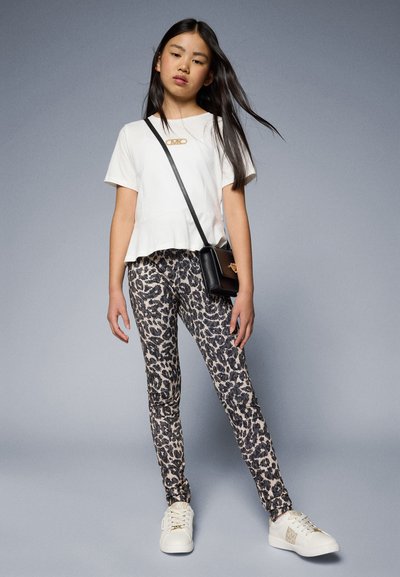 Chemise blanche à manches courtes avec un ourlet froncé, leggings imprimés léopard dans des nuances de beige et de noir, et baskets blanches avec des accents dorés.