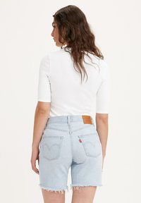 Lyseblå denimshorts med frynset kant, høj talje og særprægede baglommer med Levi's logo patch. Farve og tekstur fremhævet.