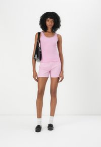 Débardeur rose côtelé avec bord en dentelle, associé à un short rayé rose. Le mannequin porte un sac à bandoulière noir, des chaussures noires et des chaussettes blanches.
