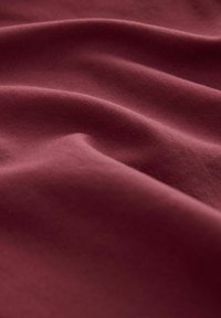 Bordo audums ar gludu tekstūru, parādot mīkstas krokas un maigu spīdumu. Materiāls izskatās viegls un nedaudz stiepjams.