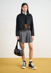 Veste noire courte avec fermeture éclair dorée, jupe plissée grise, sac bandoulière noir et baskets montantes noires avec lacets blancs.