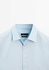 Camicia azzurro chiaro in cotone con bottoni e collo aperto, con un'etichetta nera con la scritta 'Massimo Dutti' e bottoni bianchi.