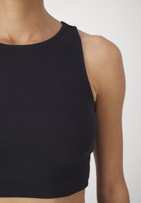 Jūros mėlynos juostuotos trumpi marškiniai su apvaliu iškirpimu, prigludęs siluetas ir be rankovių stilius. Minkšta tekstūra su minimaliai matomais siūlėmis.