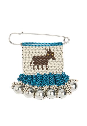 Szpilka bezpieczeństwa z obszyciem z koralików przedstawiająca brązowe zwierzę z żółtymi oczami, niebieską lamówką i srebrnymi dzwoneczkami przymocowanymi u dołu.