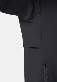 Gros plan sur la manche d'une chemise noire à manches longues et la couture latérale avec une petite poche zippée munie d'un cordon de tirage.