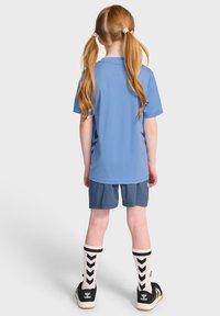 Blå sportströja med korta ärmar, tillsammans med mörkare blå shorts. Funktioner inkluderar svarta och vita mönstrade knästrumpor och svarta sneakers.
