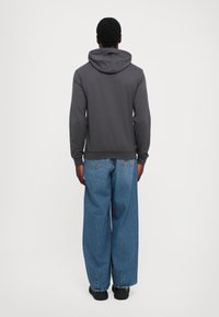 Gray hooded sweatshirt with long sleeves, ribbed cuffs, and hem, paired with loose-fitting light blue jeans and black shoes.