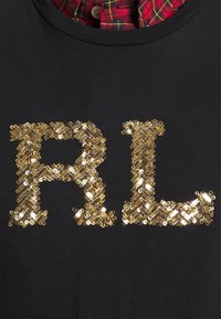 Camiseta negra con grandes letras "RL" de lentejuelas doradas brillantes y una textura suave. Capas con un cuello de camisa de cuadros rojos debajo.