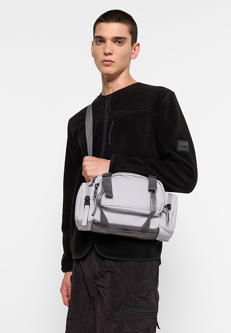 Grijze waterdichte duffel bag met twee handvatten en een schouderband, voorzien van contrasterende stiksels en meerdere gecompartimenteerde ritszakken.