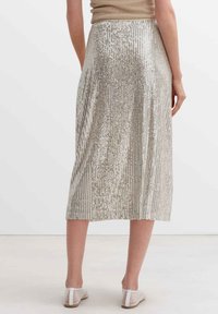 Metallic-silberner Midi-Rock mit vertikalen Paillettenmustern, elastischem Taillenbund und glatter Textur, kombiniert mit hellen Sandalen.