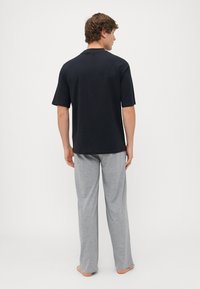 Camisa negra de manga corta y pantalones de pijama gris claro, con un corte relajado y textura suave, vistos desde la parte posterior sobre un fondo simple.