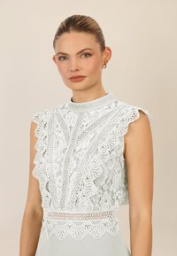 Kant crop top in licht mintgroen met golvende randen, ingewikkelde bloemmotieven en een hoge halsontwerp met een decoratieve rand.