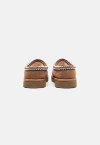 Brune semskede slip-on-sko med polstret krave, prydet med hvide og gyldne dekorative sting langs kanten og en gummisål.