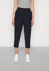 Námořnické zkrácené kalhoty vyrobené z hladkého materiálu, s bočními kapsami a elastickým pasem, doplněné bílými teniskami.