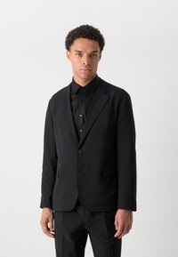 Black suit jacket with a smooth texture, single button closure, notched lapels, and a tailored fit. Paired with a matching black shirt.