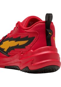 Scarpa sportiva rossa con una tomaia sintetica testurizzata, caratterizzata da un design con un fulmine nero e una suola rossa e nera prominente.